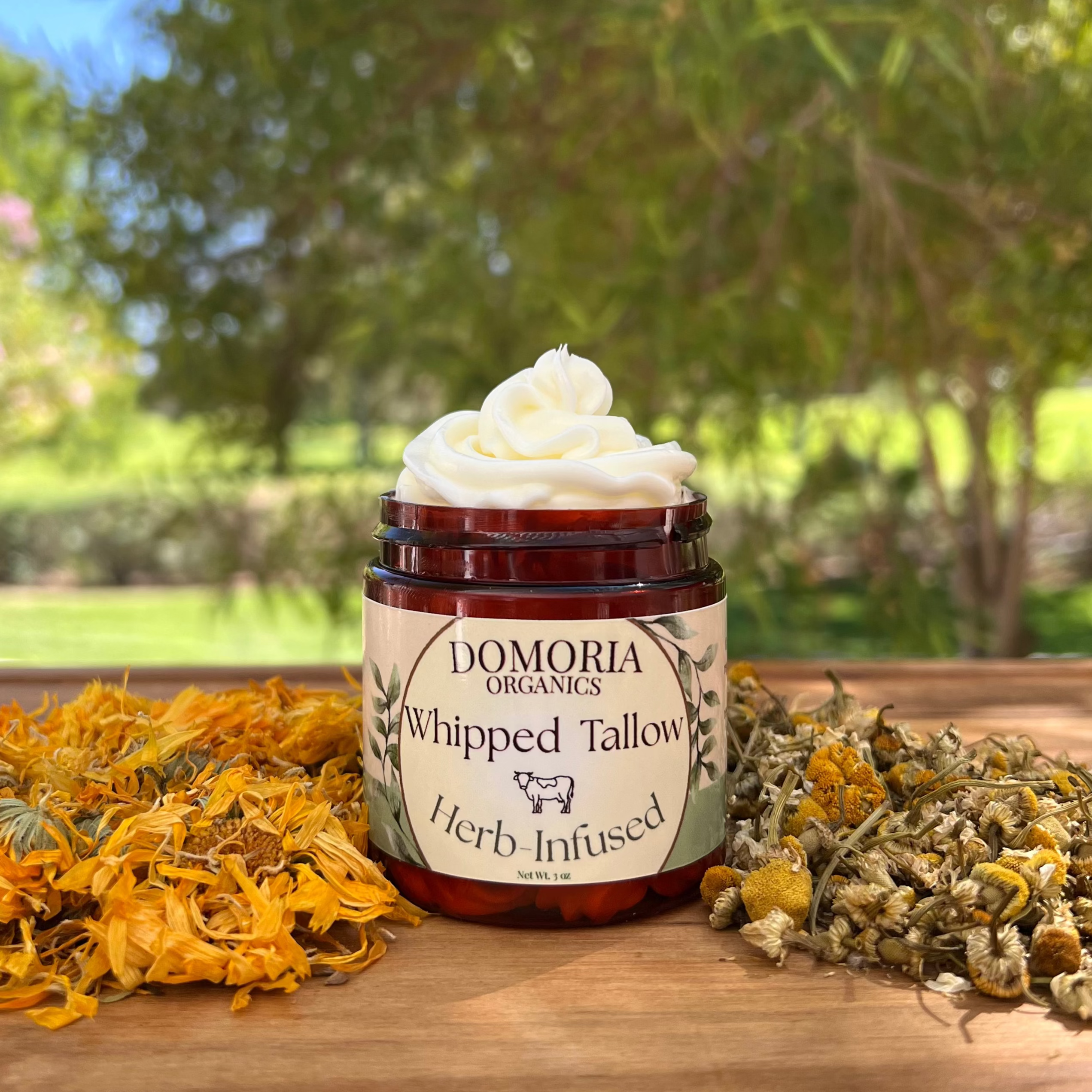 Jar of Domoria Organics Whipped Tallow with herbs on a wooden surface outdoors