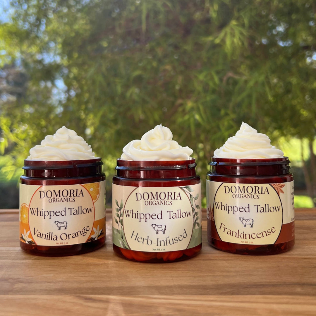 Three jars of Domoria Organics Whipped Tallow on a wooden surface with a natural background.