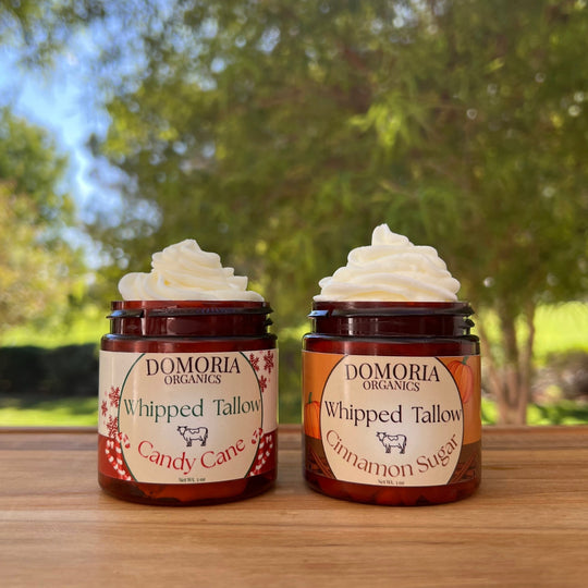 Two jars of Domoria Organics Whipped Tallow on a wooden surface with a natural background.